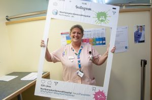 Clinical staff member at Northampton General hospital holding up selfie frame with flu messaging