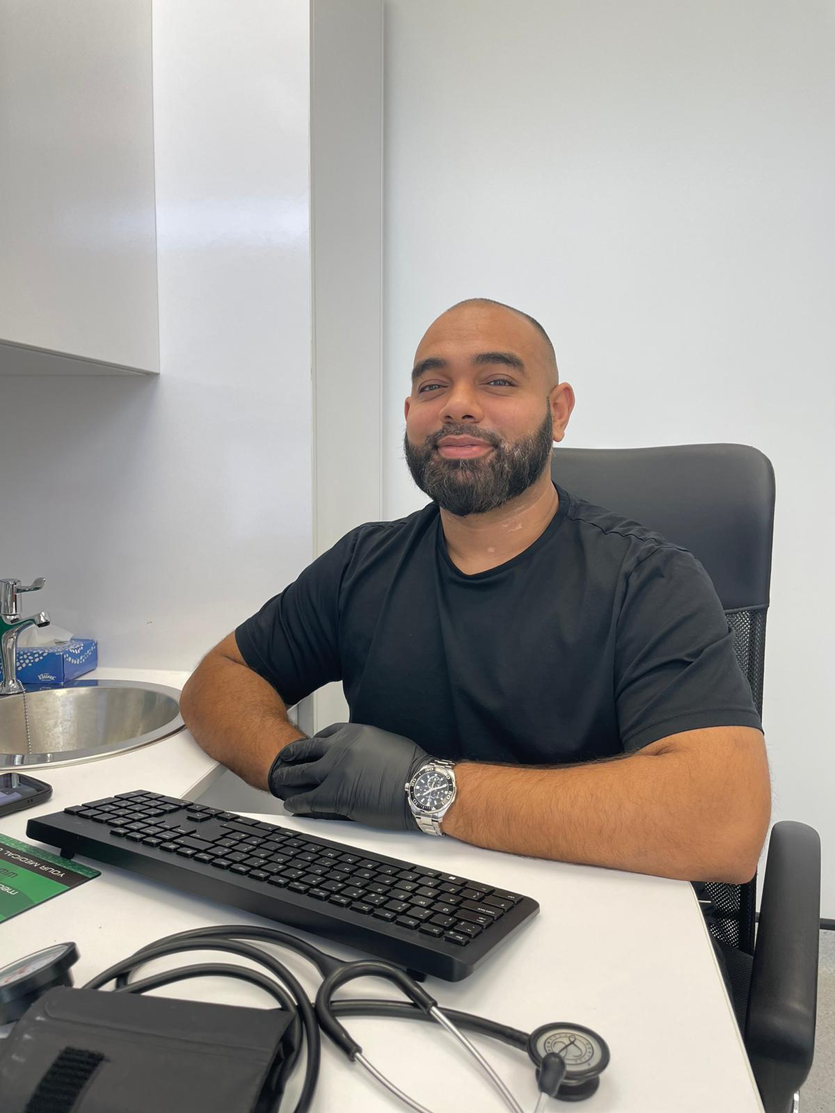Community Pharmacist Taffazzal Haque sitting at the desk in a consulting room with his computer keyboard in front of him