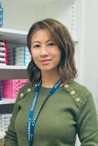 Pharmacist Zoe Chan stands in front of shelves in a pharmacy