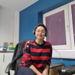 Dr Rabia Aftab leans into the camera. She is wearing a red and black striped top and is sat down at her desk.