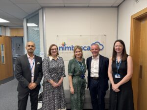 Dr Faisel Baig, Dr Emma Olandj, Professor Frankie Swords, Professor Mike Holmes and Dr Tori Blake stand in front of a wall with 'Nimbuscare' written upon it.