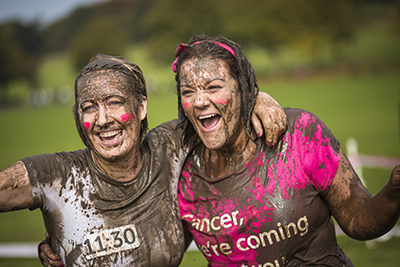 Two women muddy from a charity activity they have taken part in for a cancer charity