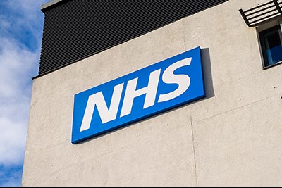 NHS logo on a wall, blue background and white italic NHS text