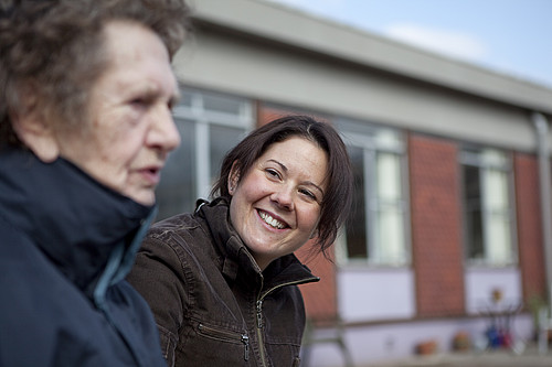 A care worker, care assistant. Staff member with a service user, an elderly woman walking with a stick. Taking a walk outside.