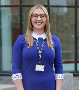 Woman wearing blue jumper and glasses looking at camera