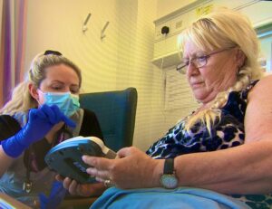 NHS nurse shows a patient how to use a medical device while she lies in bed