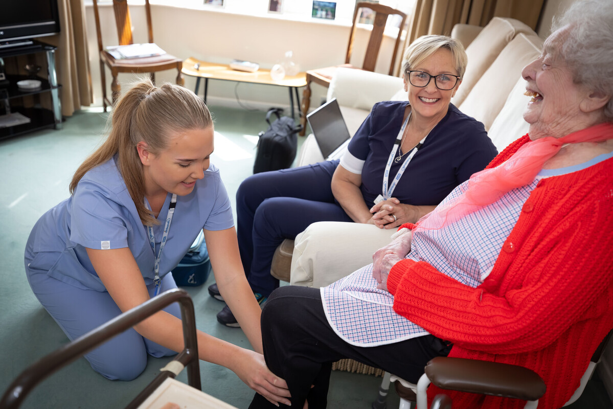 Two nurses treating older woman in her home.