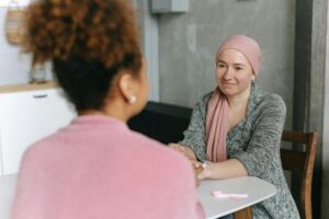 two women sat across a table from each other holding hands. One woman wears a headscarf.