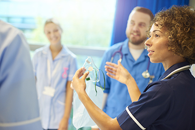 A senior staff nurse instructs a group of young male and female nurses about the oxygen breathing apparatus on the ward.