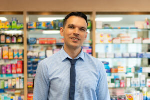 A male pharmacist standing in front of shelves with medicines on.