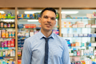 A male pharmacist standing in front of shelves with medicines on.