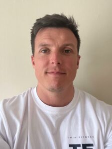 The photograph shows a head and shoulders image of a man in a white T-shirt. The man was diagnosed with testicular cancer and is helping to raise awareness of the signs of testicular cancer to look out for and when to get checked. 