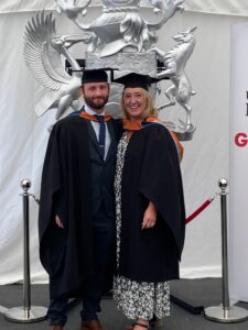 a man and a woman in graduation robes, smiling.