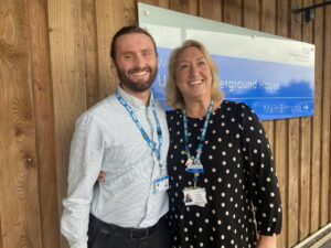 A man and a woman smiling. They are wearing NHS lanyards.