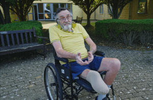 Photograph of a man in a wheelchair wearing a yellow top. His leg amputation was a result of blocked arteries caused by years of smoking. Credit Somerset Council