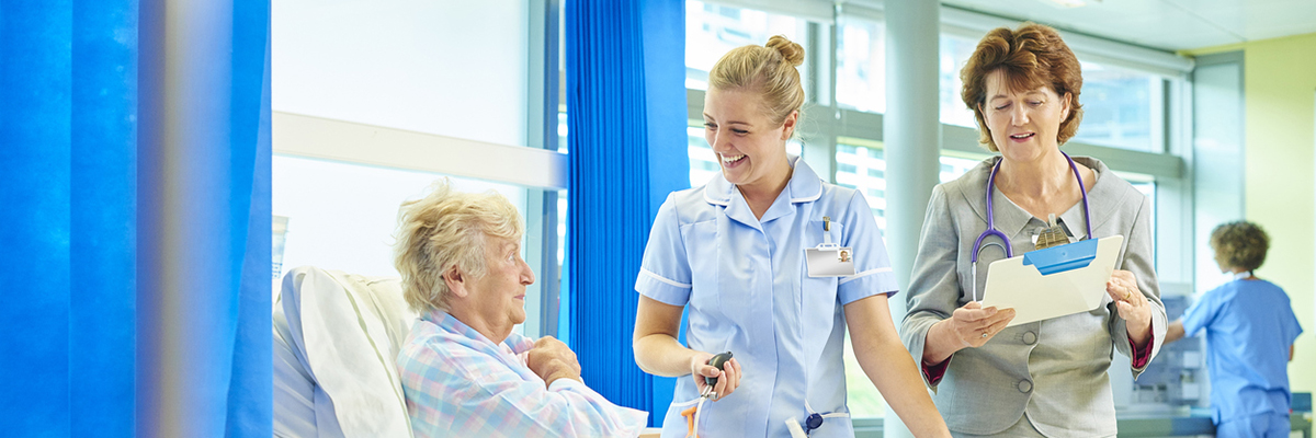 A woman in a hospital bed talks to staff