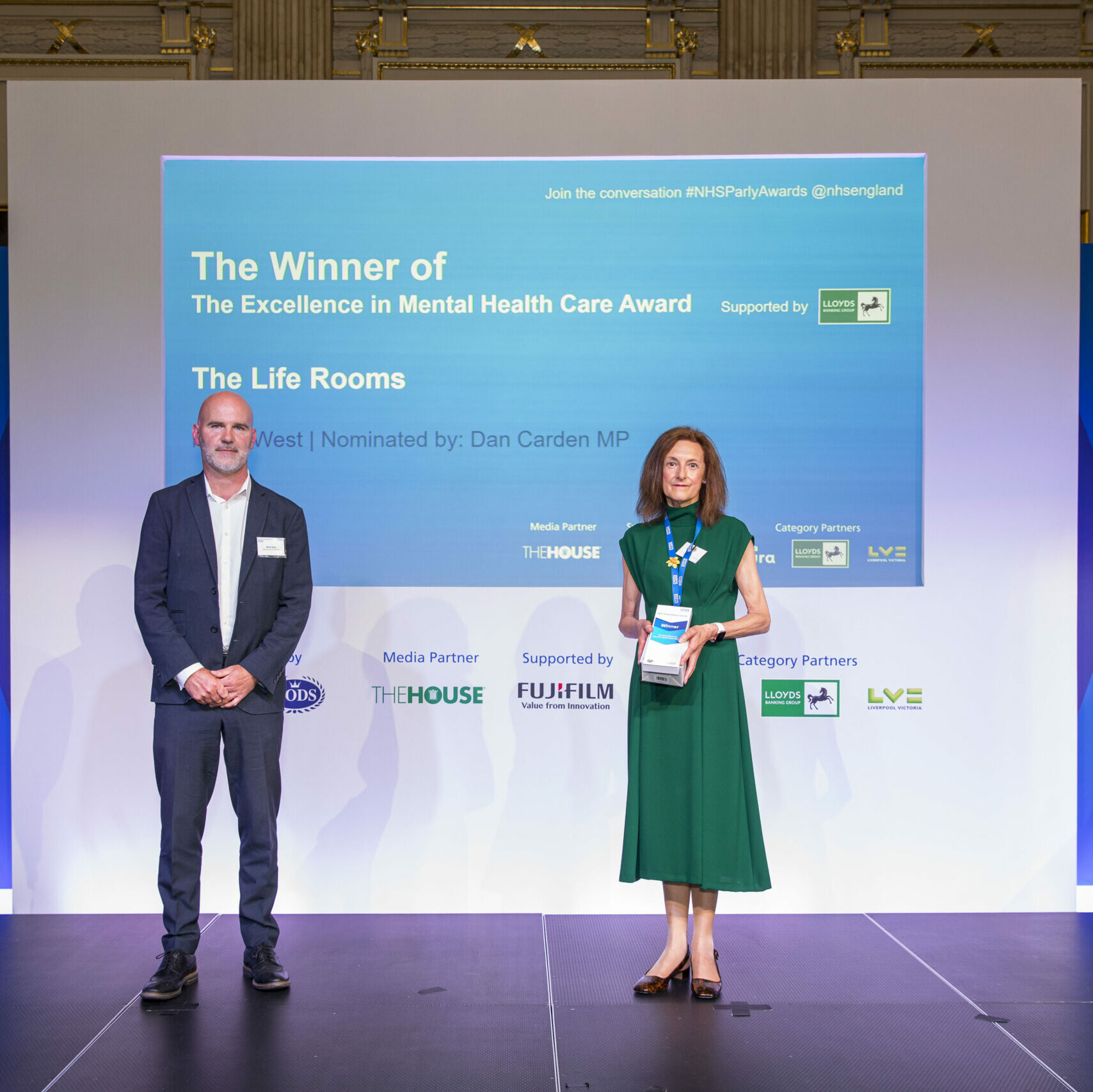 Two people are stood on the stage from The Life Rooms, Mersey Care receiving their Parliamentary NHS Award