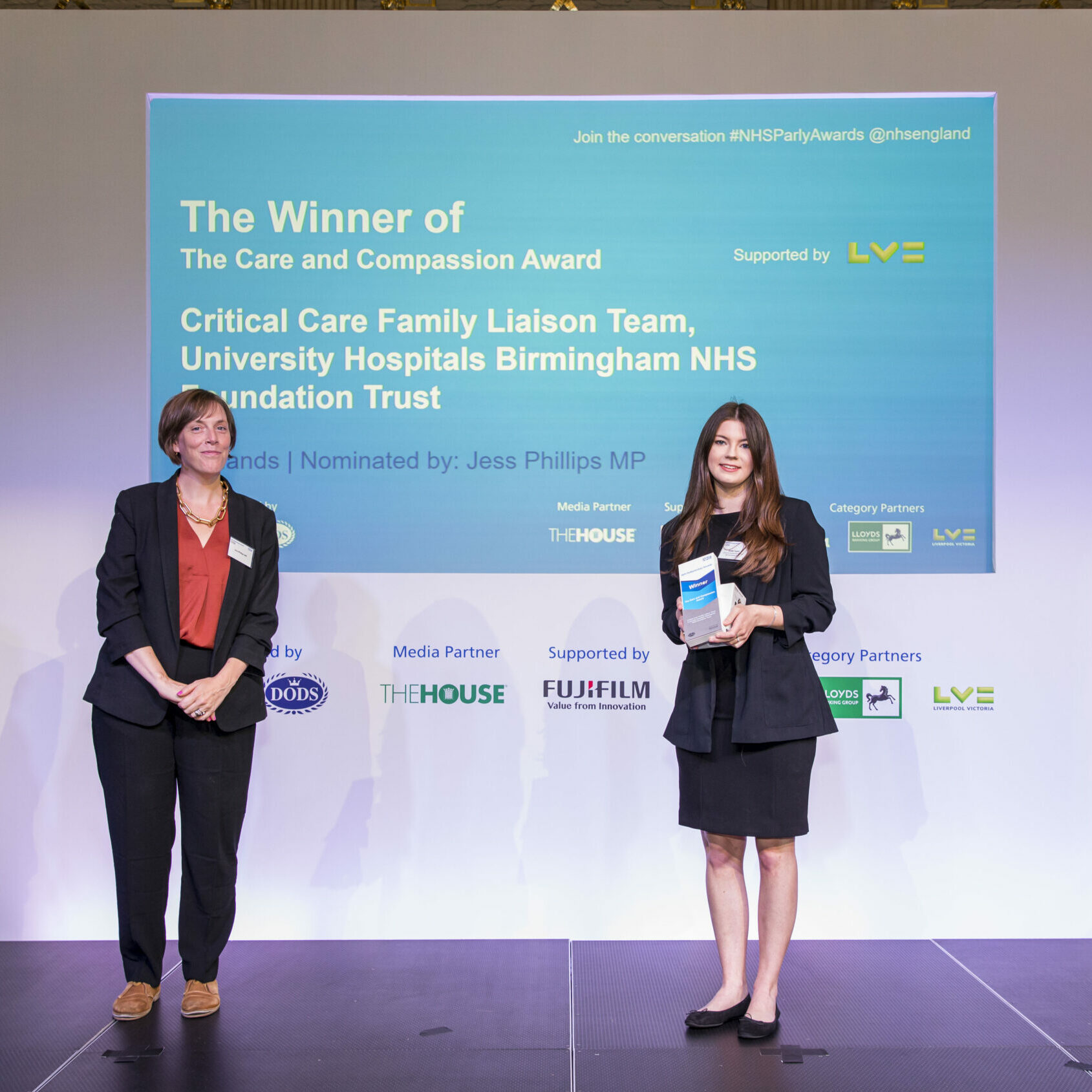 Two people are stood on a stage with a member of the Critical Care Liaison Team receiving their award