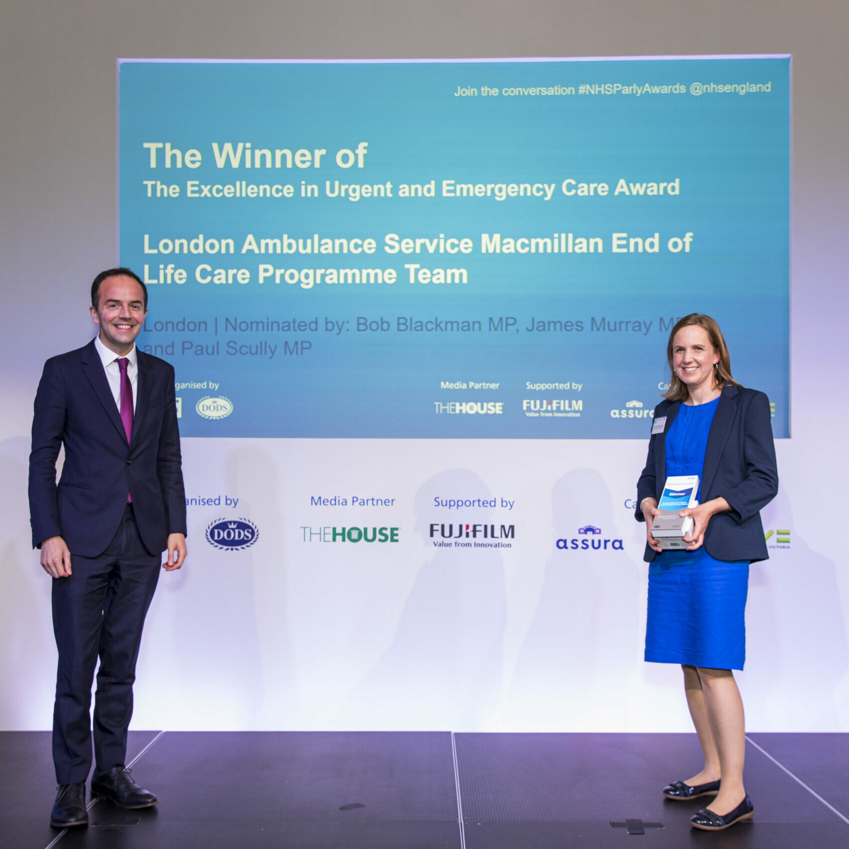 A member of the London Ambulance Service Macmillan End of Life Care Programme Team is stood on stage receiving their Excellence in Urgent and Emergency Care Award