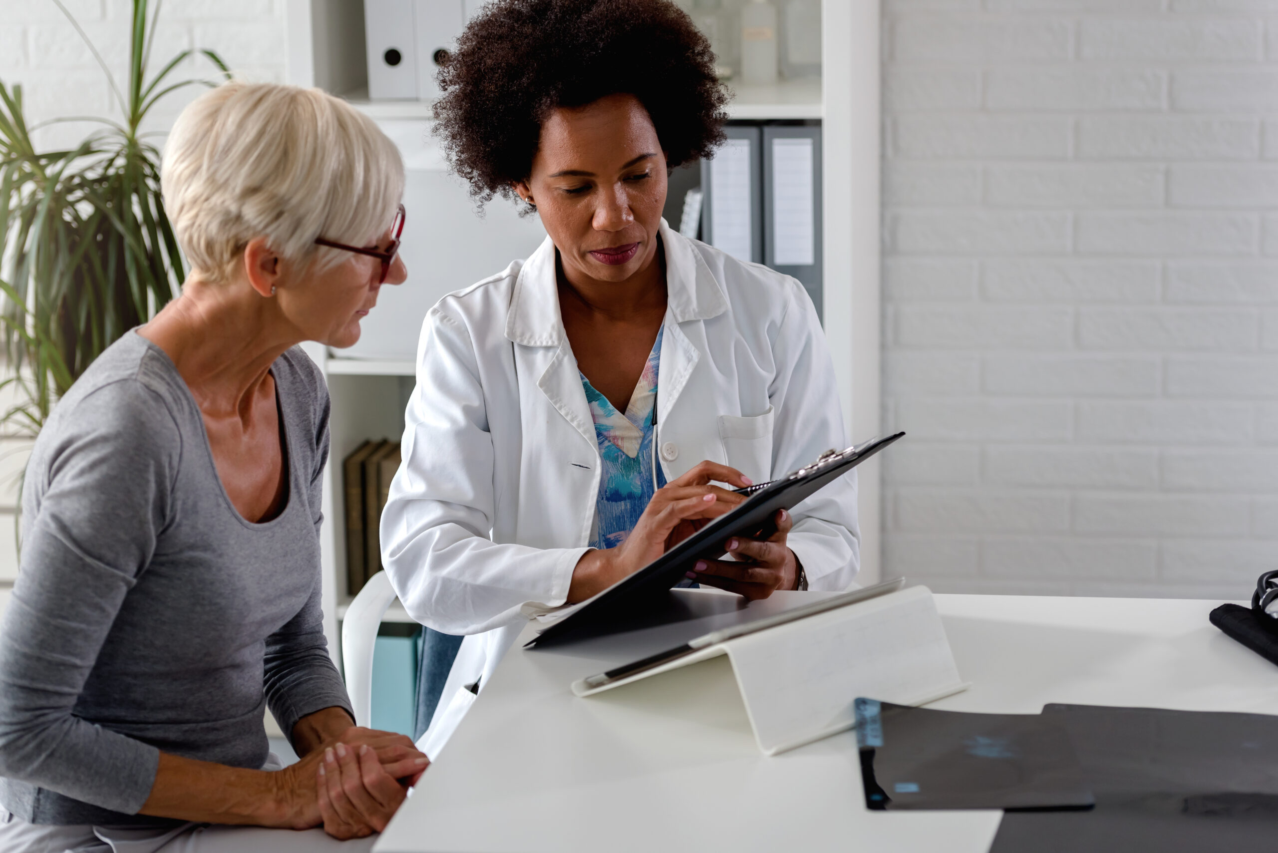 A female doctor sits at her desk and chats to an elderly female patient while looking at her test results