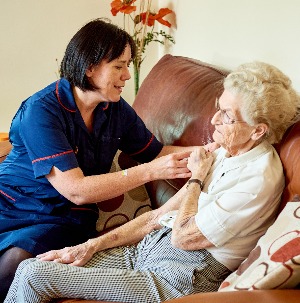 Photograph of a healthcare professional providing care to a patient in their own home.