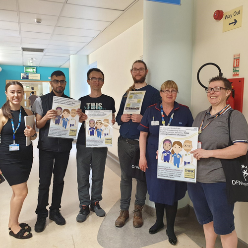 Six healthcare staff in a hospital corridor displaying 'Learning Disabilities Champion' posters