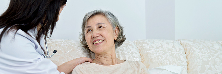 Female doctor talking to senior patient in hospital bed.