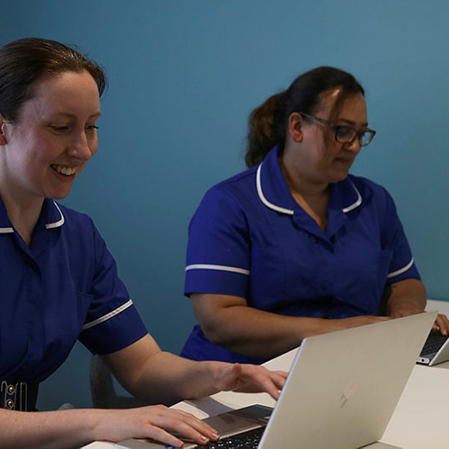 Two nurses sat together using laptops