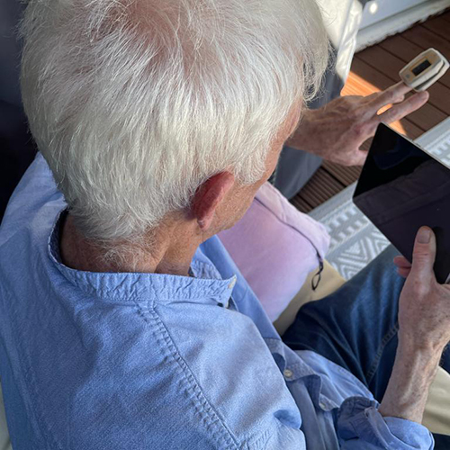 Older man taking his own temperature and holding a digital device