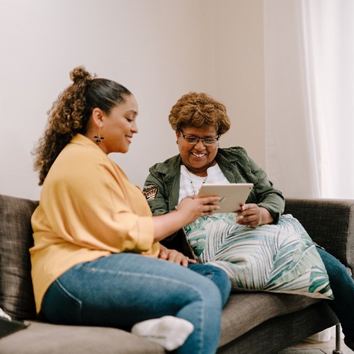 Two women sitting on a sofa looking at a tablet