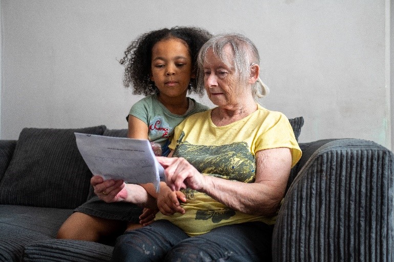 A photo of an elderly woman reading information off a sheet and being cuddled by a young girl.