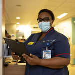 Photo of Lily Onoh working in a hospital holding a clipboard and wearing a face mask