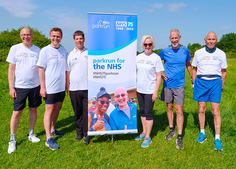 Parkrun launch - a group of runners standing by a parkrun banner. Runners include Professor Sir Stephen Powis and Dame Ruth May DBE.
