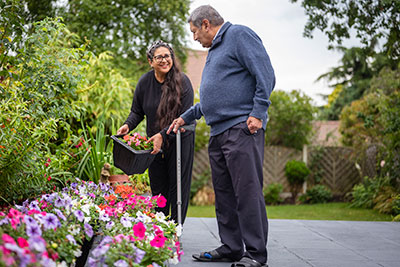 Man with a walking stick talking a women who is gardening