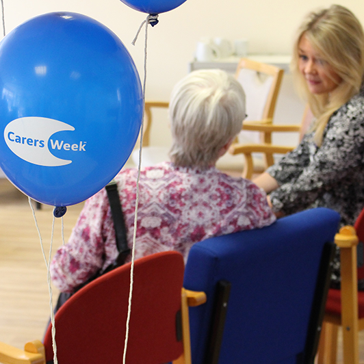 Older person and carer sitting down and talking together. Blue 'careers week' balloon in foreground.