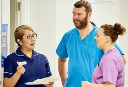 A group of male and female healthcare colleagues have a discussion within a healthcare setting
