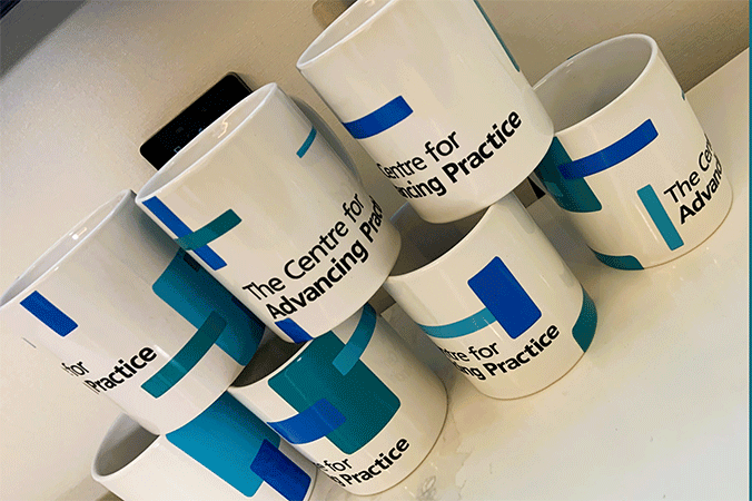 Row of fours mugs with a row of 3 mugs stack on top. The mugs have Centre for Advancing Practice written on them.